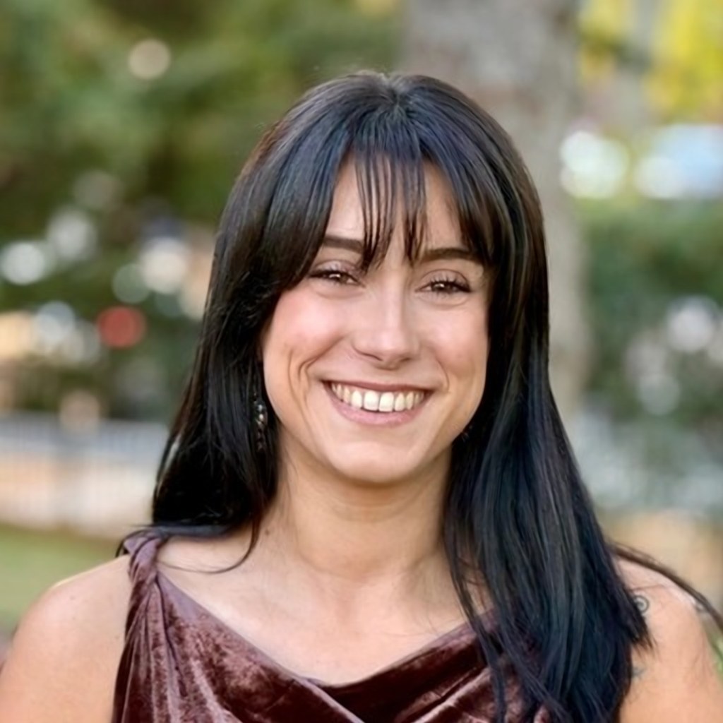 Becca, smiling outdoors with long dark hair